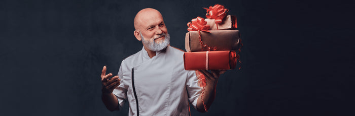 A cook holding a stack of wrapped gift boxes filled with Christmas gifts for chefs