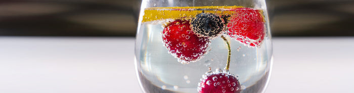 A close-up of a bubbly soda garnished with cherries, berries, and a lemon