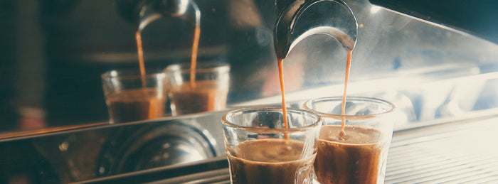 Shots of espresso being dispensed by an espresso machine into two glasses 