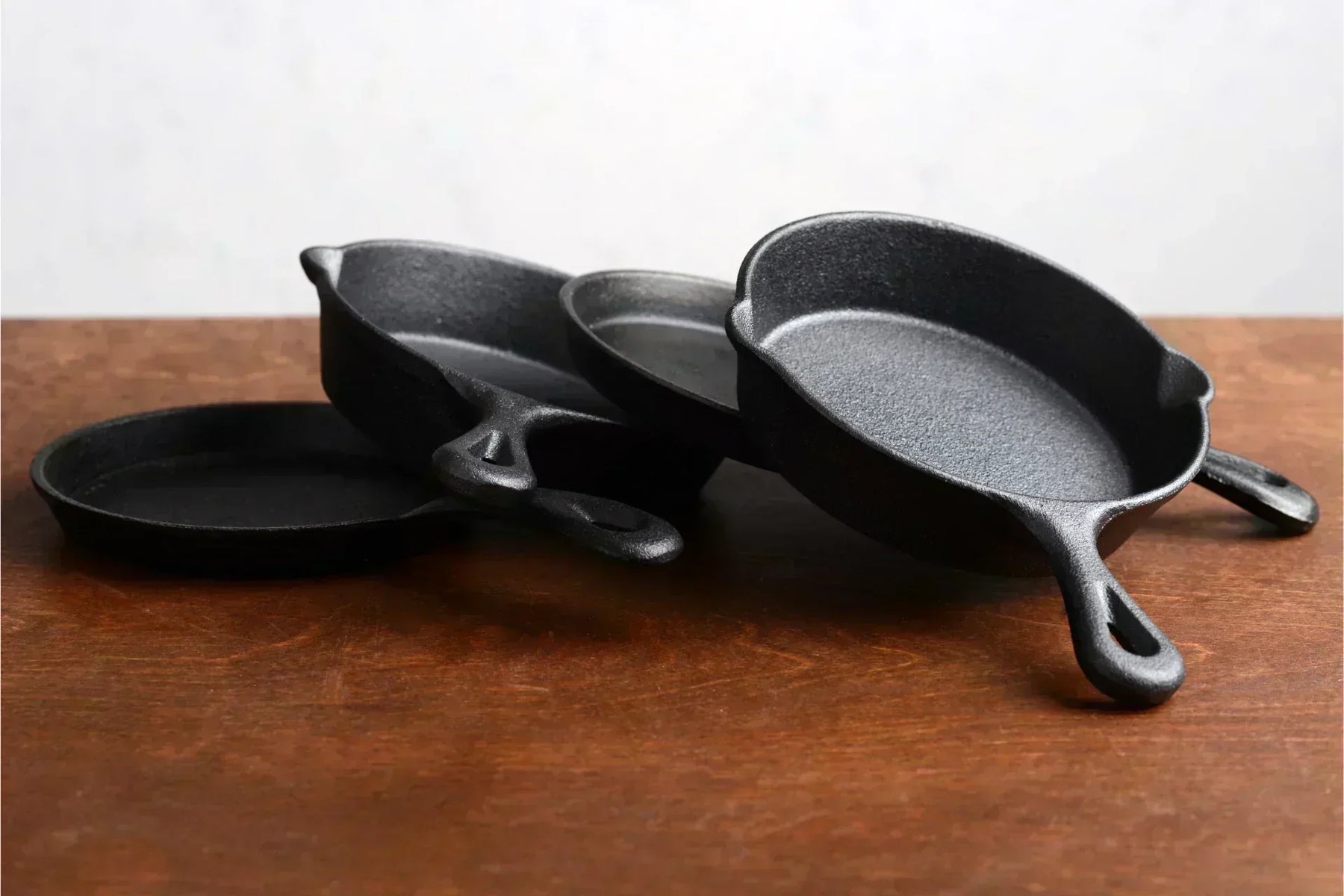 Stack of black cast iron skillets with handles overlapping, resting on a wooden surface against a light background
