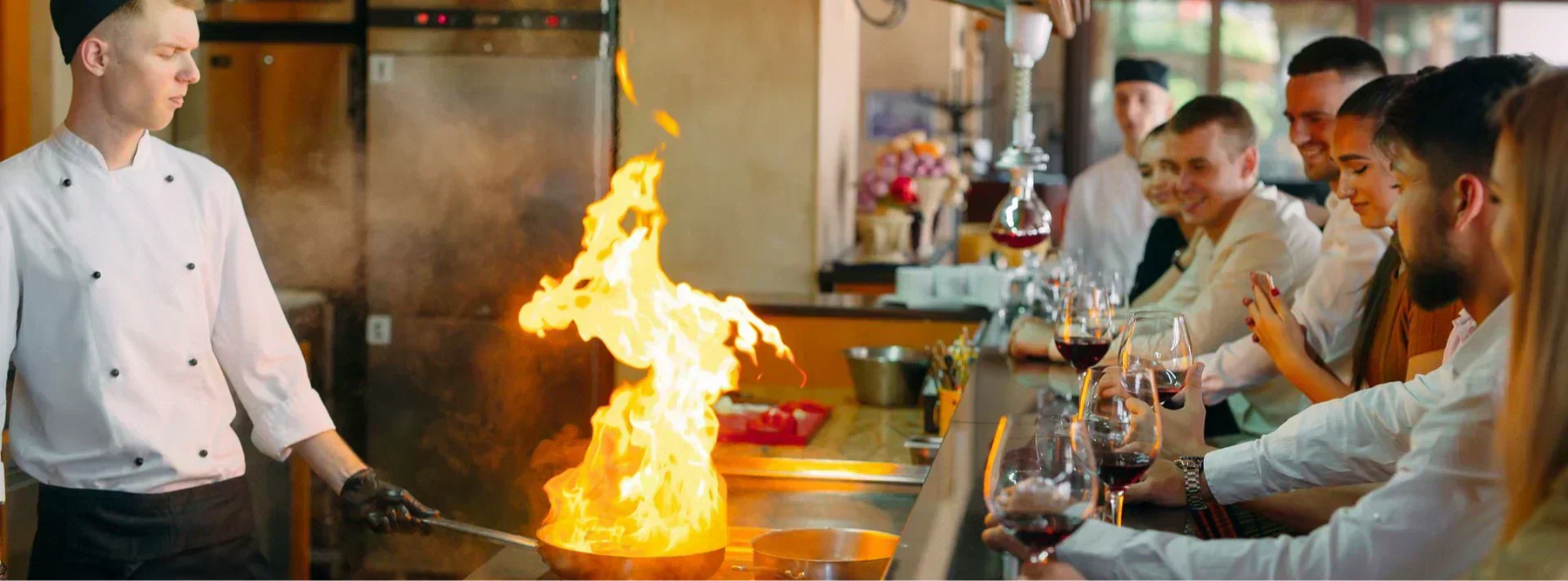 A line cook preparing food in an open kitchen with guests watching and dining in front