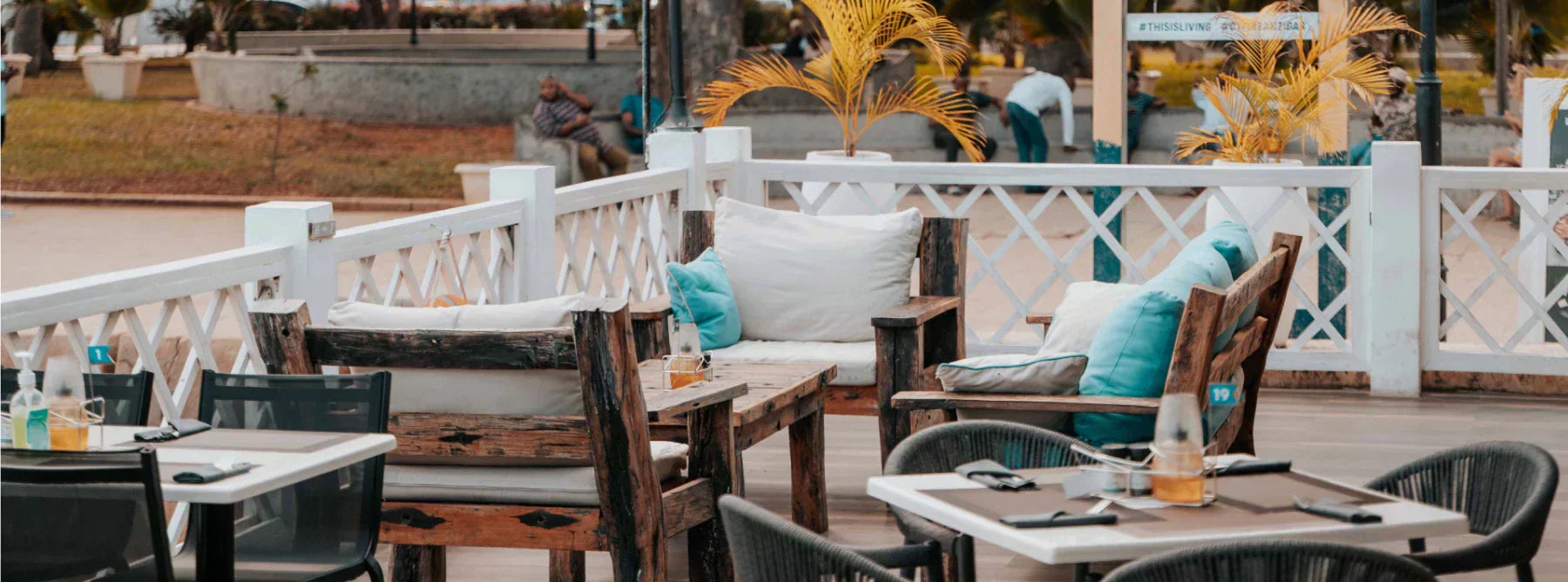 Commercial patio furniture setup at an outdoor restaurant with wooden tables, cushioned chairs, and wrought iron furniture.