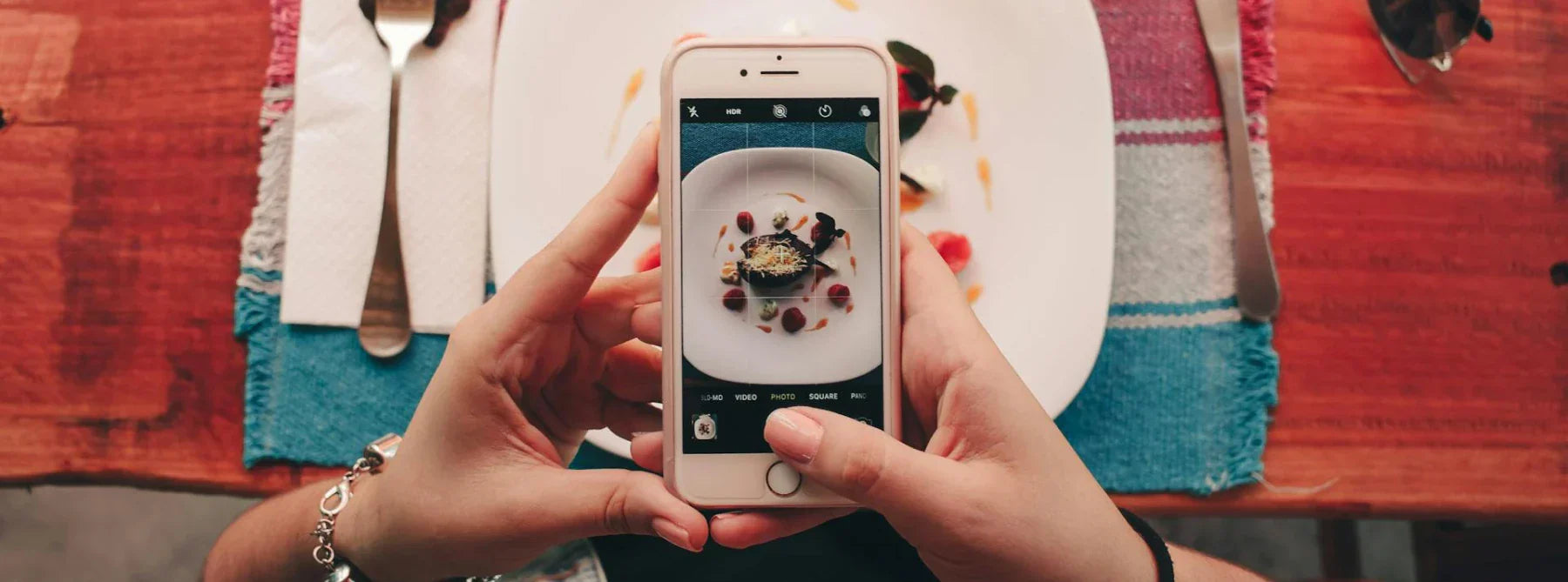  A person taking a picture of a meal on a table, with utensils on the sides, a drink and sunglasses nearby