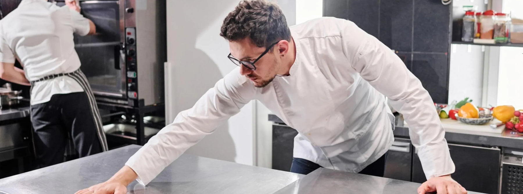 Kitchen staff cleaning a work station table with a stainless steel finish.