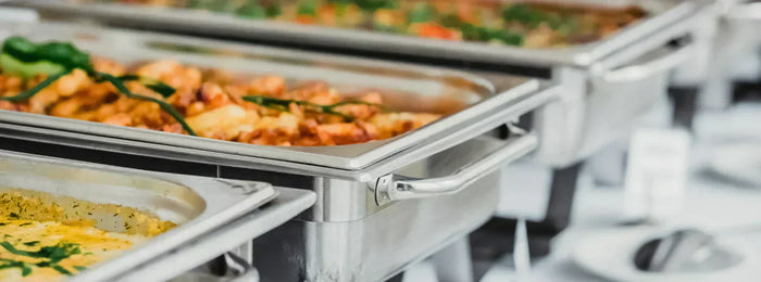 A close-up shot of a catering equipment setup with chafing dishes lined up on a clothed table