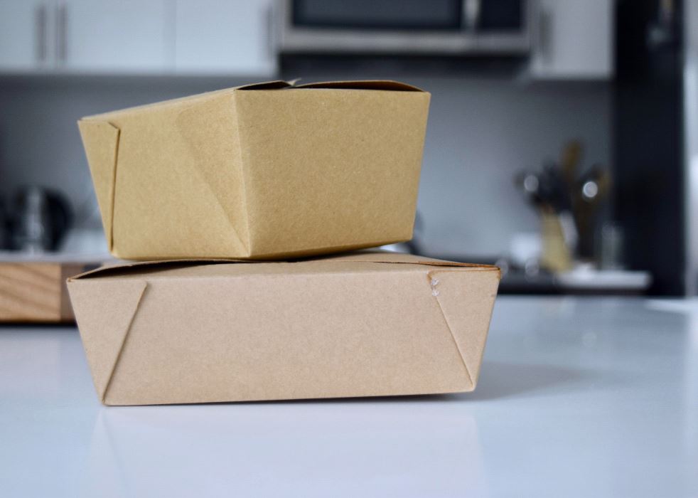 Two takeout boxes stacked on top of eachother on kitchen counter