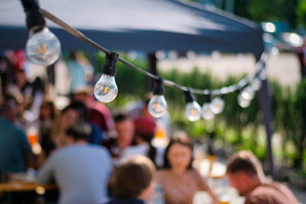 String lights hang in the foreground of a large outdoor BBQ event