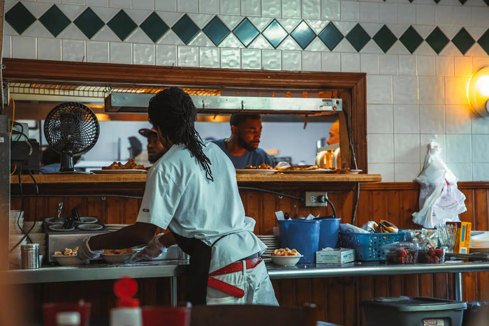 A male chef grabs food bowls while looking through a kitchen window at his colleagues. 
