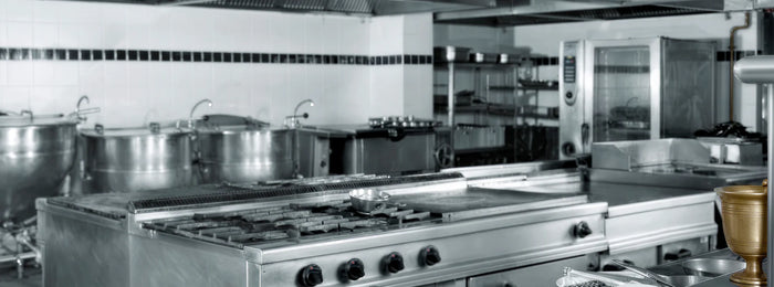 Commercial kitchen with stainless steel appliances, industrial stoves, and ventilation hoods for restaurant cooking.