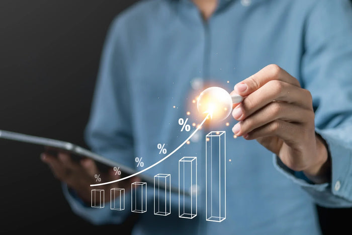 Person holding a tablet and pointing at a glowing upward-trending bar chart with percentage symbols, representing revenue growth