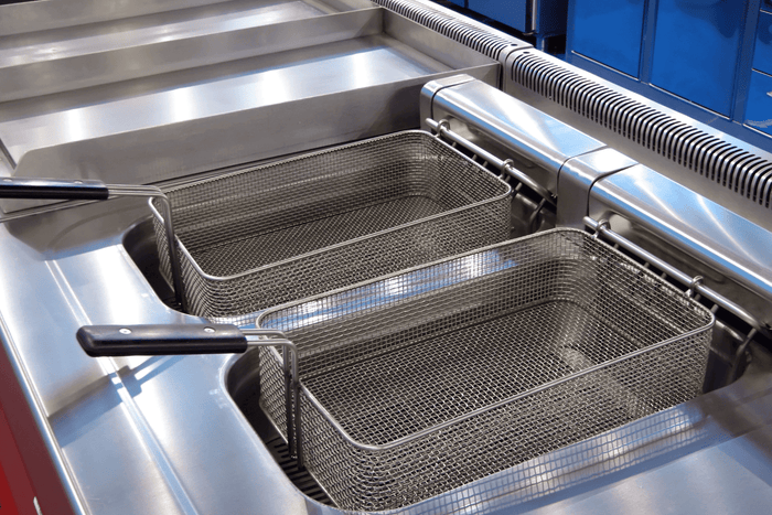 Close-up of a stainless steel commercial deep fryer with two empty wire baskets and black handles, ready for cooking.
