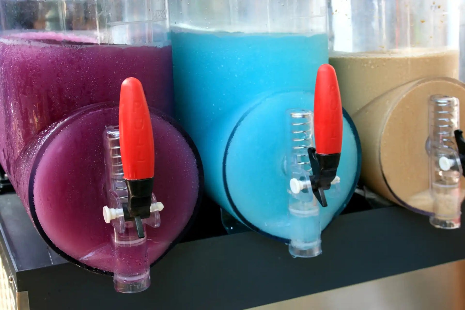 Three slush machine models are lined up at a convenience store filled with a range of flavours. 