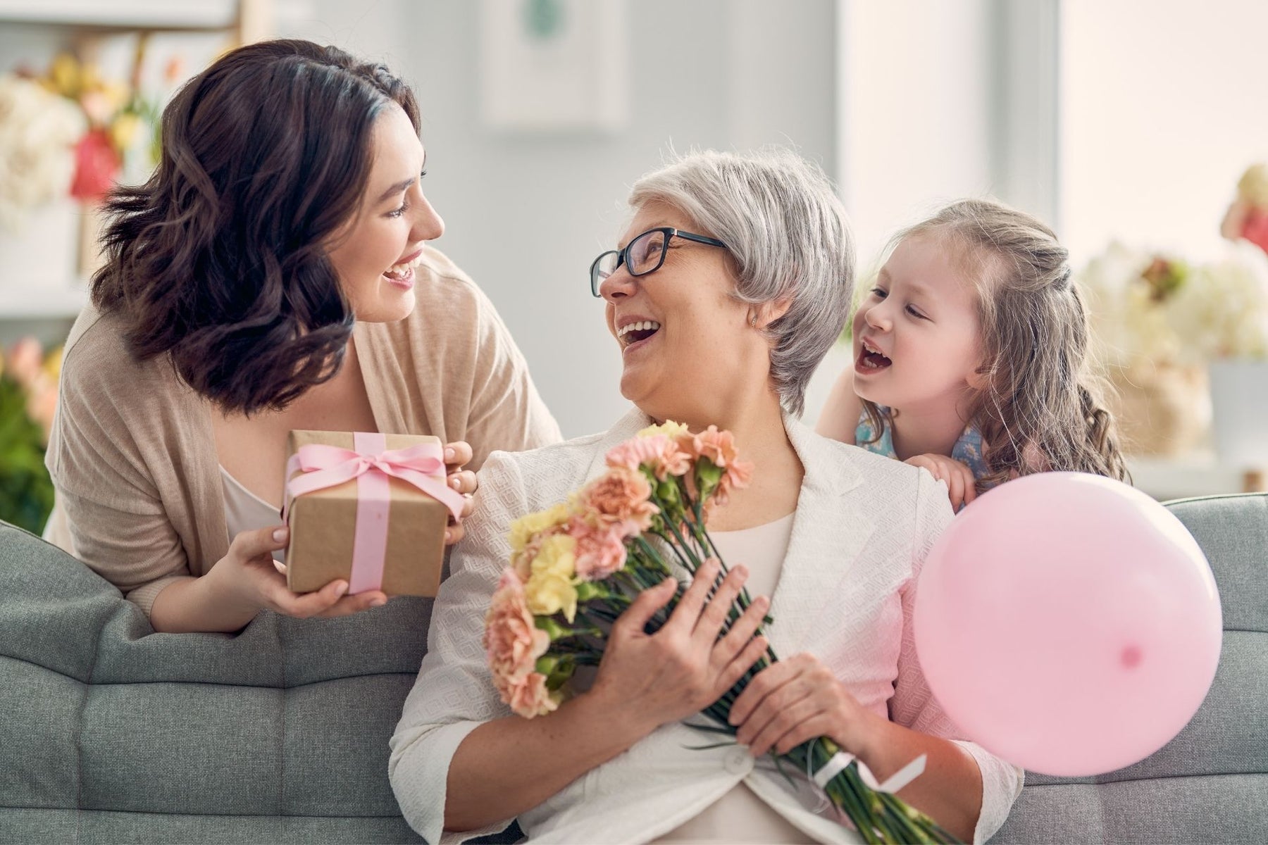A mother and daughter surprising a grandmother with a gift, flowers, and a balloon 