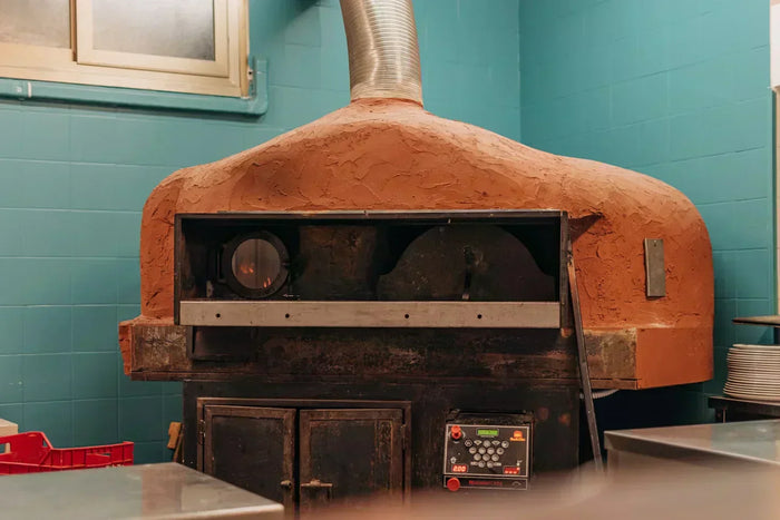 An antique orange bakery oven stands in front of blue brick walls. 