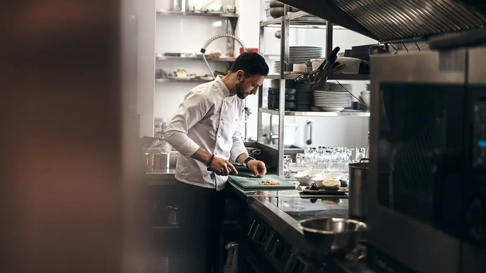 A male chef cuts vegetables in a kitchen packed with utensils, cookware and appliances. 