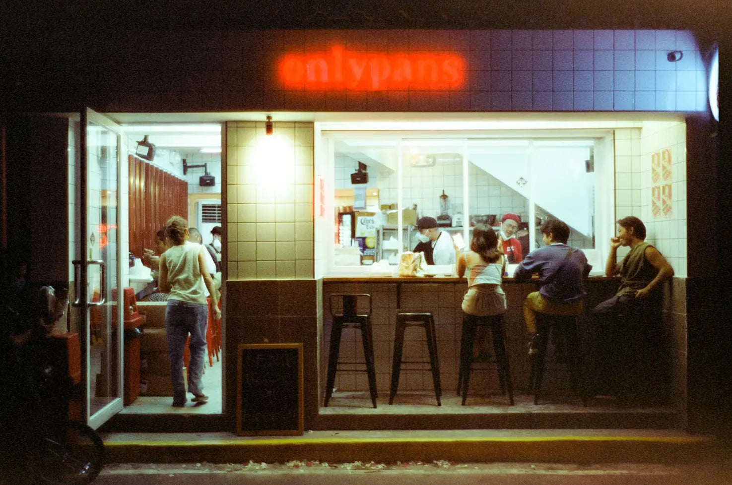 Grainy, 90s-style diner photo of customers eating outside its window, with cooks visible inside. 