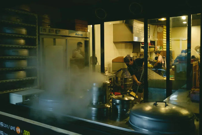 Looking over a kitchen counter,  an employee mops the floor while another washes a sink.